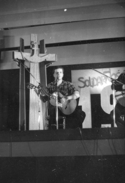 Jacek Kaczmarski podczas koncertu. W głębi krzyż (makieta pomnika Poległych Stoczniowców 1970) oraz transparent "Solidarności", 31 sierpnia 1981 r. (AIPN)