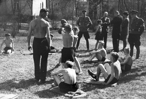 Uczniowie szkoły Hitlerjugend podczas zajęć bokserskich. Widoczni chłopcy i oficerowie przyglądający się walce dwóch chłopców. Fot. NAC