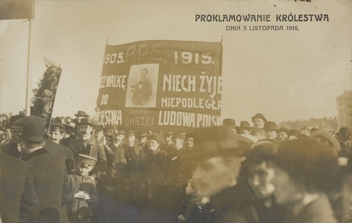 Pocztówka z fotografią dokumentalną, w której w tłumie ludzi trzymany jest transparent PPS ze zdjęciem Stefana Okrzei. Fot. Biblioteka Narodowa