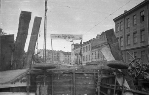 Barykada pomiędzy budynkami na ulicy Okopowa 33 (róg Barona) i Okopowa 26. Z tyłu po prawej wdoczny wylot ul. Wolność (nazwa okupacyjna ul. Zegarmistrzowska). Nad barykadą napis na transparencie: "Barykada im. Stefana Okrzei. AK, sierpień 1944". Fot. Wikimedia Commons