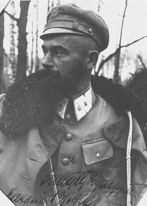 Edward Rydz-Śmigły w okresie służby oficerskiej w Pierwszej Brygadzie Legionów Polskich. Na zdjęciu jest stosunkowo młody mężczyzna z obfitymi, zakręconymi na końcach ku górze wąsami i dużą kozią brodą, w mundurze oficera Legionów Polskich w armii austriackiej podczas I wojny światowej, z zarzuconym na ramiona płaszczem wojskowym z grubym, czarnym kołnierzem, mający na głowie czapkę z przypiętym do niej polskim orłem legionowym, stojący na tle zagajnika. W czasie, gdy Józef Piłsudski i Kazimierz Sosnkowski przebywali w twierdzy magdeburskiej, Edward Rydz-Śmigły przejął kierownictwo nad Polską Organizacją Wojskową. Widząc korzystny moment polityczny, wezwał do Lublina galicyjskich polityków niepodległościowych, a po powołaniu 7 listopada 1918 roku rządu - objął w nim tekę ministra wojny.