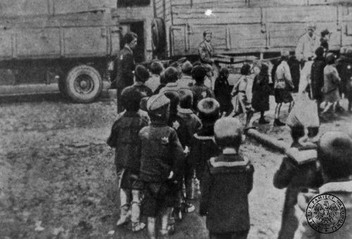 Grupa małych dzieci żydowskich idzie parami na jednej z ulic Łodzi podczas deportacji do obozu zagłady w Chełmnie nad Nerem latem 1942 r. Fot. AIPN