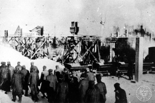 Grupa więźniów KL Auschwitz maszeruje zimą przed elementami konstrukcji budowanej, 1942-1943 r. Fot. AIPN