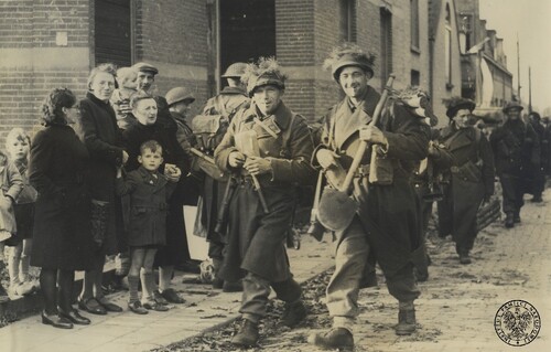 Polscy żołnierze piechoty z 1. Dywizji Pancernej idący ulicą w wyzwolonej Bredzie, 29 października 1944 r. Żołnierz po prawej niesie dużą saperkę i zawieszony na ramieniu potrójny zasobnik na pociski do ręcznego granatnika przeciwpancernego PIAT. Po lewej grupa witających Polaków holenderskich cywilów (kobiety, dzieci). Fot. z zasobu IPN