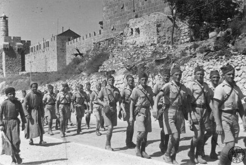 Wzdłuż murów Jerozolimy, podczas zwiedzania miasta, maszerują żołnierze 3. baterii Dywizjonu Strzelców Górskich Brygady Strzelców Karpackich, 29 lipca 1940. Żołnierze są w mundurach francuskich. Idą m.in.: kan. Roman Chadalski (piąty z lewej, w furażerce i chustce na karku), kan. Górecki (ósmy z prawej), kan. Jarecki (szósty z prawej), kapral Janiszewski (czwarty z prawej). Na ostatnim planie starożytne mury Jerozolimy i Brama Jafska (z lewej). Fot. z zasobu IPN