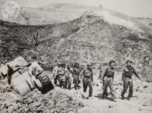 Polscy żołnierze niosą i prowadzą rannych. Na drugim planie klasztor na Monte Cassino. Po lewej stronie: zniszczony czołg M4 Sherman