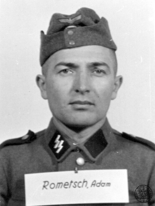 Zdjęcie portretowe gładko ogolonego, krótko ostrzyżonego mężczyzny w mundurze ze znakiem „SS” na prawym kołnierzu munduru i w czapce z niemieckim nazistowskim orłem. Na wysokości piersi tabliczka ze słowami: „Rometsch, Adam”.