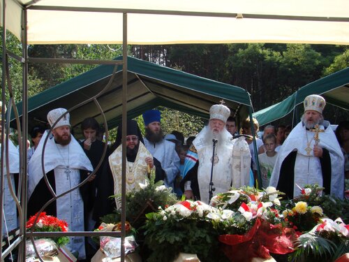 Mężczyźni w strojach liturgicznych duchownych prawosławnych stoją nad trumnami przykrytymi wieńcami
