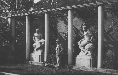 Mężczyzna pozujący do zdjęcia pomiędzy dwiema rzeźbami pomnikowymi