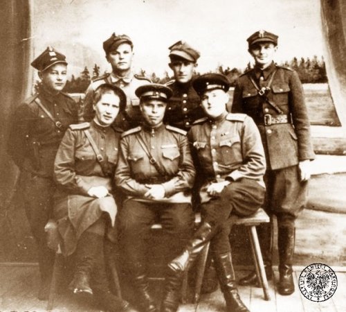 Pozowane zdjęcie siedmiu osób: czterech mężczyzn stoi z tytułu, mają na sobie mundury wojskowe polskiego kroju, troje pozostałych, wśród nich kobieta, nosi mundury sowieckie i siedzi z przodu