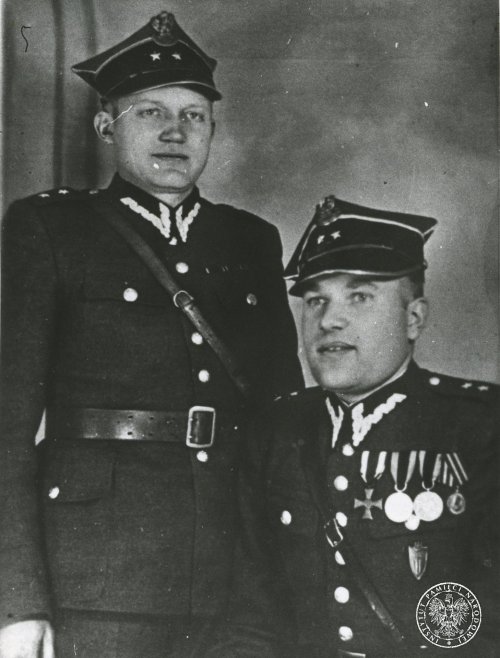 Dwóch mężczyzn w mundurach typu polskiego; jeden z mężczyzn ma przypiętych na mundurze kilka odznaczeń