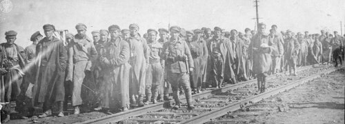 Żołnierze w zwartej kolumnie zebrani przy linii torów kolejowych.
