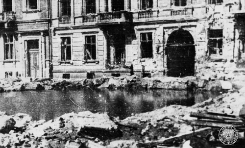 Wypełniony wodą krater po wybuchu pocisku niemieckiej ciężkiej artylerii na podwórzu kamienicy w czasie Powstania Warszawskiego. Fot. z zasobu IPN