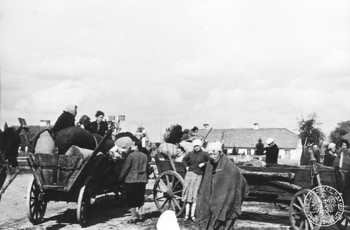 Wrzesień 1939 roku w zajętym przez oddziały niemieckie Czerwinie koło Ostrołęki. Wozy konne, na których i przy których siedzą i stoją zmęczeni polscy wojenni uchodźcy cywilni, prawie same kobiety. Na wozach worki z dobytkiem, który udało się uchodźcom wziąć. W tle zabudowania.