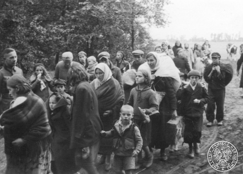 Wrzesień 1939 roku. Duża grupa polskich, cywilnych uchodźców wojennych, w tym dzieci, idących z tobołkami polną drogą. Grupie przypatruje się niemiecki żołnierz.
