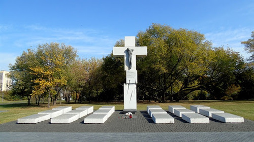 Założenie pomnikowe: duży, biały, trzyczęściowy krzyż z figurą Ukrzyżowanego Chrystusa, pod nim, w dwóch grupach po obydwu stronach, po 9 białych tablic/płyt. W tle rozłożyste drzewo