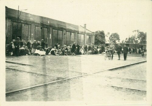 Ludzie w oczekiwaniu na transport na teren Generalnego Gubernatorstwa, w tle hala nr 1. Źródło: Muzeum Dulag 121/depozyt Bożeny Sławińskiej