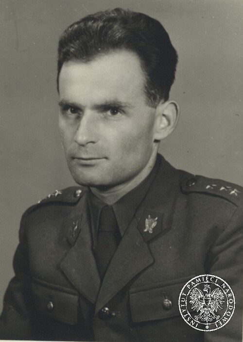 Mężczyzna o pociągłej twarzy, z lekko pofalowanymi, czarnymi włosami, w mundurze oficera (kapitana) skrojonym na wzór polski