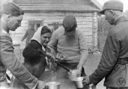 Kobieta nakłada jedzenie do metalowych misek żołnierzom oddziału partyzanckiego Armii Krajowej [?] w jednej z wsi w okupowanej Polsce, 1942-1944. Fot. z zasobu IPN