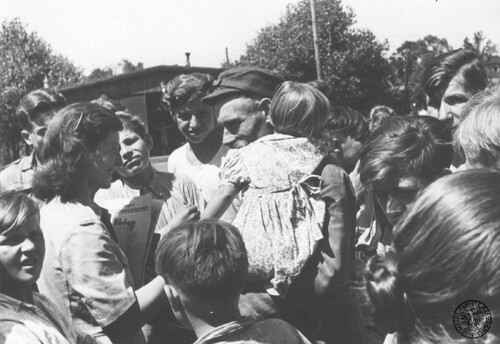 Dorrit Camil, przedstawicielka Organizacji Narodów Zjednoczonych do Spraw Pomocy i Odbudowy (UNRRA) (2L) w rozmowie z mężczyzną (w czapce), który odnalazł w jednym z transportów repatriacyjnych z Niemiec pięcioro swoich dzieci; 1945 - 1946. Fot. z zasobu IPN