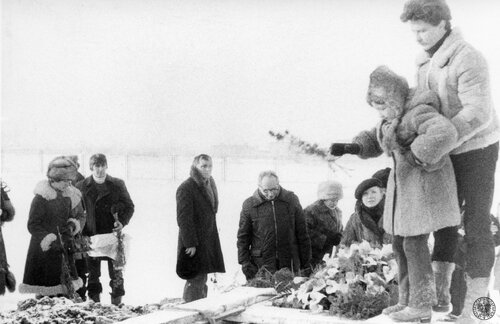Pogrzeb Ryszarda Gzika, jednego z górników zamordowanych przez reżim Jaruzelskiego podczas pacyfikacji KWK „Wujek”; Na grobie mężczyzna trzyma dziewczynkę, Agnieszkę Gzik - córkę zabitego, która składa kwiaty. 21 grudnia 1981 r., cmentarz w Katowicach-Piotrowicach przy ul. Dąbrowszczaków (obecnie Armii Krajowej). Fot. z zasobu IPN