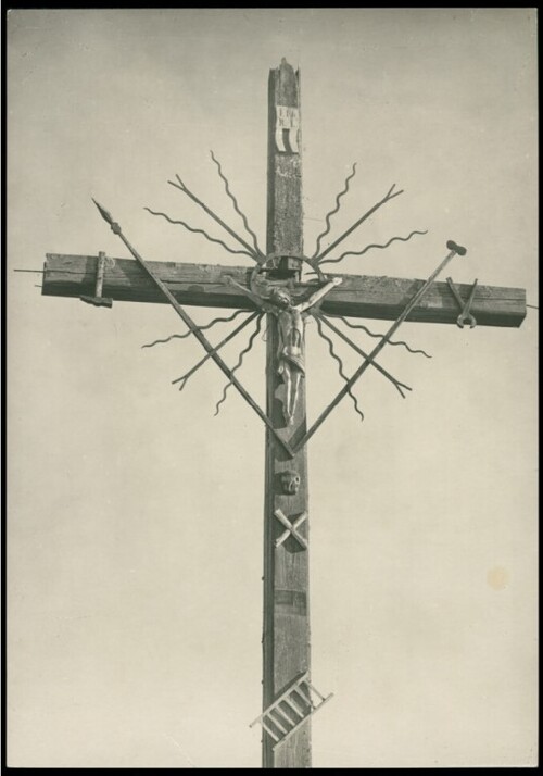 Drewniany krzyż Chrystusowy w polu, gdzieś za Brasławiem, przed 1930 rokiem. Na krzyżu metalowa figura Ukrzyżowanego oraz powieszone metalowe imitacje narzędzi kaźni dokonanej na Jezusie Chrystusie przez Jego oprawców.
