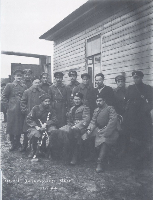 Stanisław Bułak-Bałachowicz ze swoim sztabem, październik-listopad 1919 roku. Grupa żołnierzy, oficerów, umundurowanych na wzór rosyjski, stoi lub siedzi pod drewnianym budynkiem.
