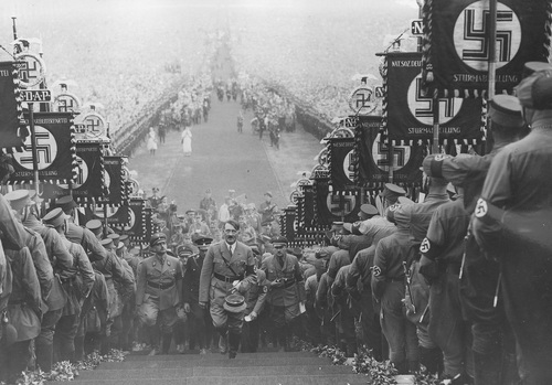 Adolf Hitler podczas uroczystości dożynkowych w otoczeniu oficerów wchodzi na górę Buckeberg pod Hameln przez szpaler utworzony z partyjnych sztandarów. Na drugim planie widoczny wielotysięczny tłum, 30 września 1934 r. Fot. NAC