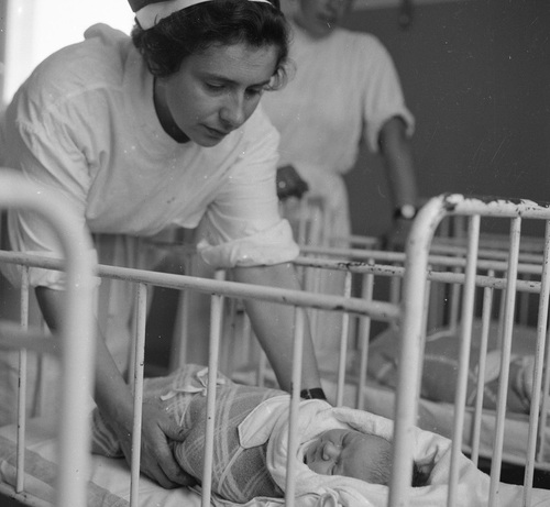 Położna pochylona nad noworodkiem leżącym w łóżeczku, 1962 r. Fot. NAC