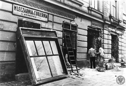 Tworzenie getta na terenie krakowskiego Podgórza, marzec 1941. Dwóch mężczyzn zamurowuje otwór okienny obok „Mleczarni i Cukierni” Rosenfelda. Fot. z zasobu IPN