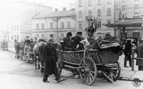 Plac Zgody (dziś Plac Bohaterów Getta) w Podgórzu w marcu 1941 r., w czasie tworzenia niemieckiego getta dla krakowskich Żydów. Na placu stoją drewniane wozy konne załadowane meblami. Na ostatnim planie kamienice stojące przy placu. Fot. z zasobu IPN