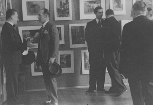Mężczyźni w małych grupach w sali wypełnionej obrazami na ścianach
