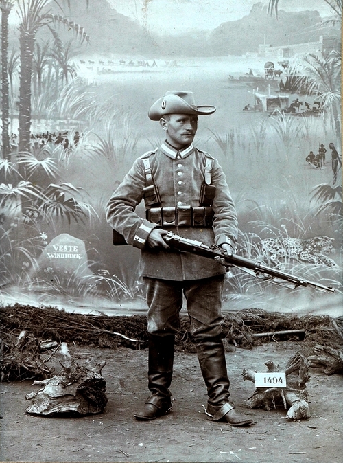 Mężczyzna pozujący do zdjęcia w charakterystycznym umundurowaniu z bronią w ręku