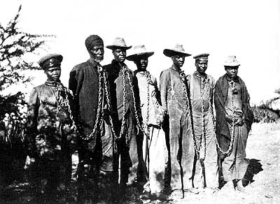 Grupa ustawionych do zdjęcia czarnoskórych mężczyzn skutych łańcuchami