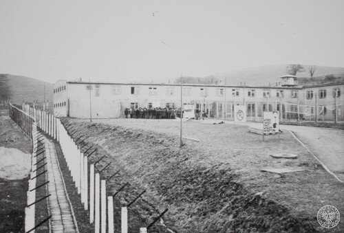Akcja protestacyjna osób internowanych w Ośrodku Odosobnienia w Uhercach, 19 kwietnia 1982 r. Zakład Karny w Uhercach z podwójnym ogrodzeniem. Przed budynkiem stoją internowani. Zdjęcie wykonane prawdopodobnie z wieży strażniczej. Fot. z zasobu IPN