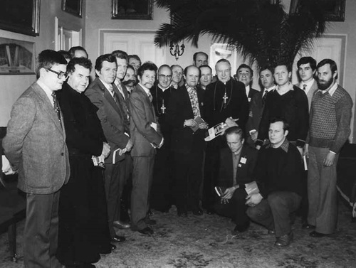 Grupa kilkunastu mężczyzn w otoczeniu księdza kardynała w elegancko urządzonym pomieszczeniu