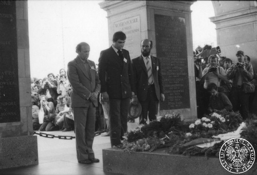 Trójka mężczyzn z pochylonymi głowami stojących przed Grobem Nieznanego Żołnierza po złożeniu wieńca. W tle tłum fotoreporterów