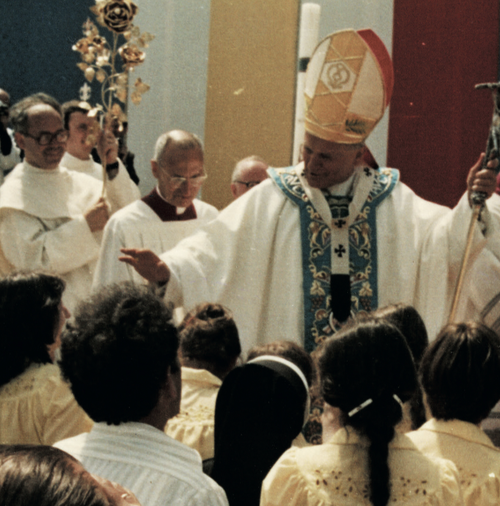 Mężczyzna w katolickim stroju liturgicznym otoczony przez grupę osób