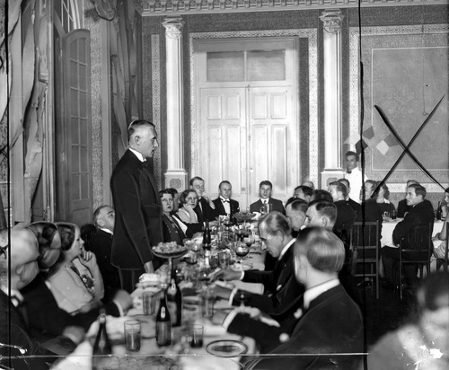 Podczas bankietu Władysław Raczkiewicz w pozycji stojącej przemawia do zasiadających przy stole osób.