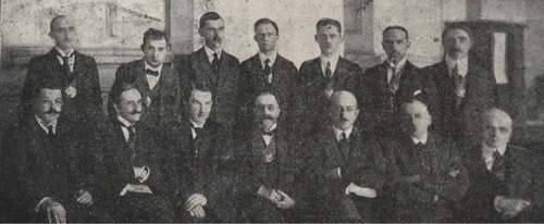 Grupa eleganckich mężczyzn ustawionych do zdjęcia w dwóch rzędach. Pierwszy rząd siedzi.