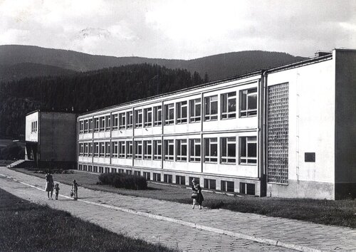 Na archiwalnym zdjęciu budynek szkolny o charakterystycznych cechach architektonicznych: zbudowany z betonu, niskopiętrowy, na ogólnym planie prostokąta.