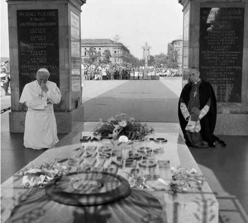 Dwóch mężczyzn w strojach duchownych katolickich (białym - papieskim i ciemnym) klęczy przy płycie pamiątkowej Grobu Nieznanego Żołnierza