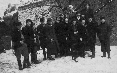 Grupa kilkunastu osób - kobiet i mężczyzn, którzy z uśmiechem pozują do zdjęcia, stojąc pod drzewem. W tle kamienny mur.