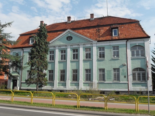 Współczesne zdjęcie budynku o stylowej architekturze. Elewacja w odcieniach zieleni. Dach pokryty dachówką.