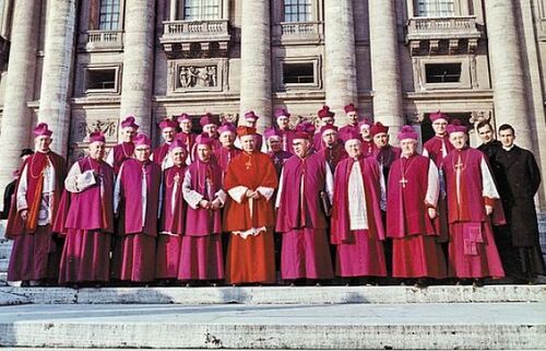 Grupa mężczyzn w strojach hierarchów katolickich pozuje do zdjęcia na stopniach przed frontonem zabytkowego kościoła