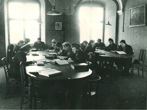 Studenci przy owalnych stołach podczas lektury książek w czytelni.