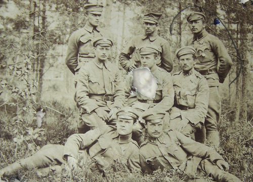 Grupa 8 mężczyzn w mundurach pozujących do zdjęcia na leśnej polanie