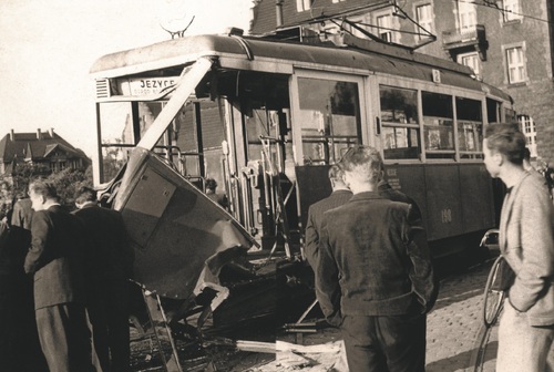 Kilka osób stojących wokół zniszczonego tramwaju.