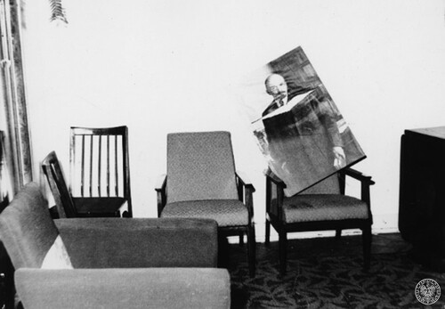 Pomieszczenie, w nim jeden duży fotel, dwa mniejsze i dwa krzesła; częściowo widoczne biurko. Na jednym z mniejszych foteli położono uszkodzony portret Lenina.