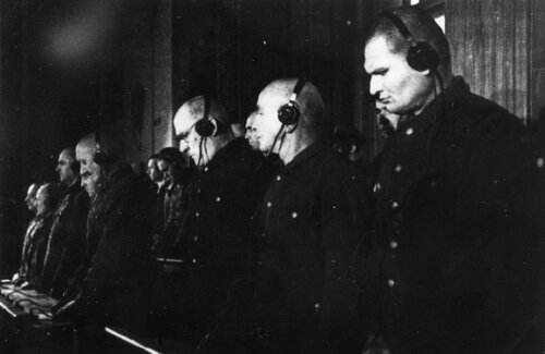 Grupa byłych członków załogi KL Auschwitz-Birkenau stoi na ławie oskarżonych podczas ogłaszania wyroku - zbliżenie pod kątem